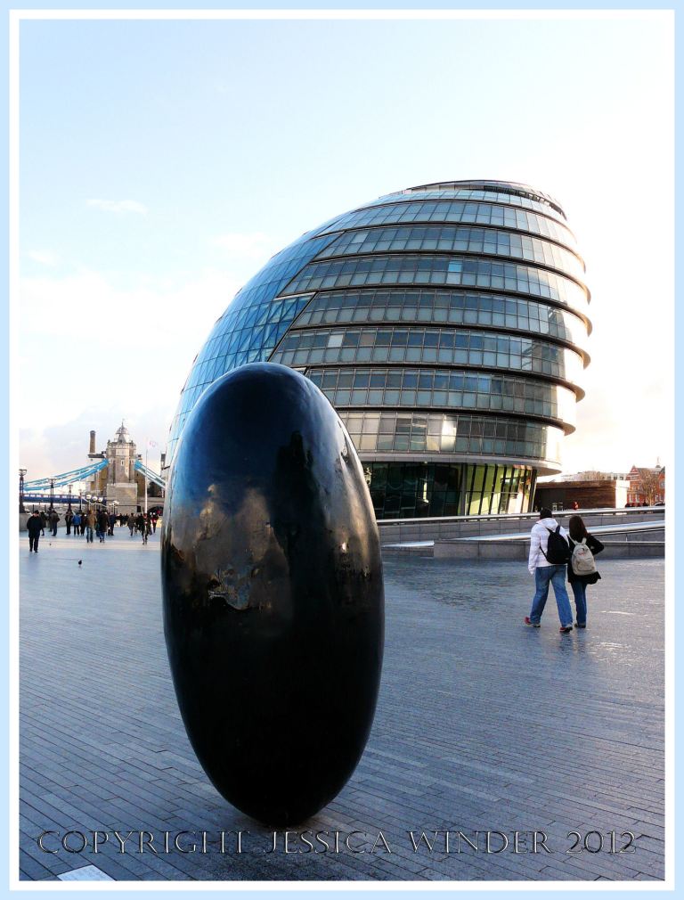 Black egg shaped sculpture on the South Bank, London, UK, close to a lop-sided snail shaped building occupied by City Hall.