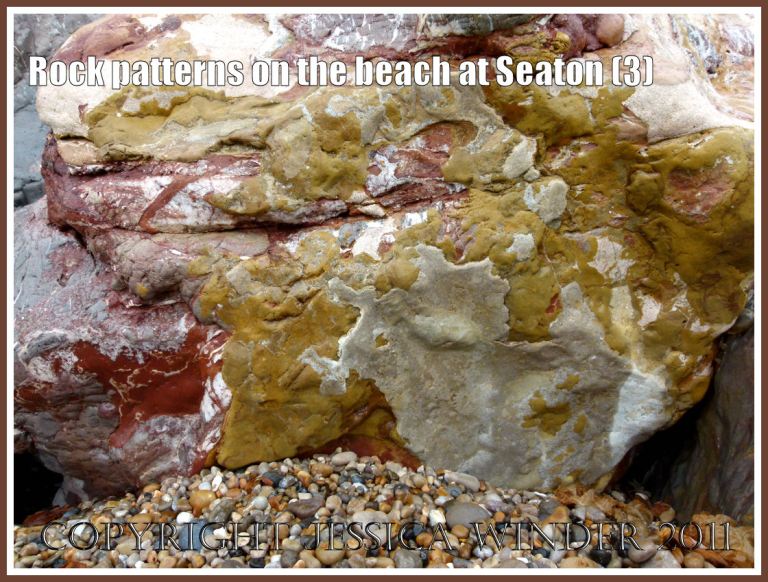 Rock pattern: Natural geological abstract pattern in red, yellow, and buff on the side of a large boulder that forms part of the rock armour preventing erosion on the beach at Seaton, Devon, U.K. - part of the Jurassic Coast World Heritage Site (3)