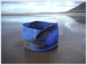 Blue plastic improvised crate with rope handles washed up on sandy beach.