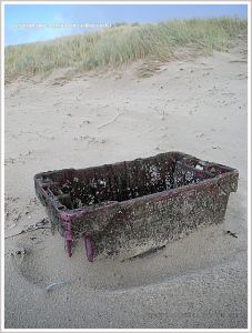 Red fishing crate washed up as flotsam on sandy beach