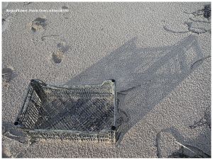 Black plastic crate and shadow on sandy beach