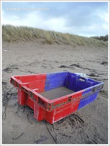 Red and blue fishing crate flotsam on beach