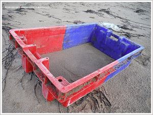 Red and blue fishing crate flotsam on beach
