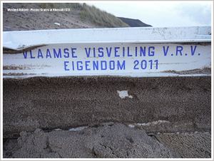Detail of white plastic crate with blue writing washed up on beach