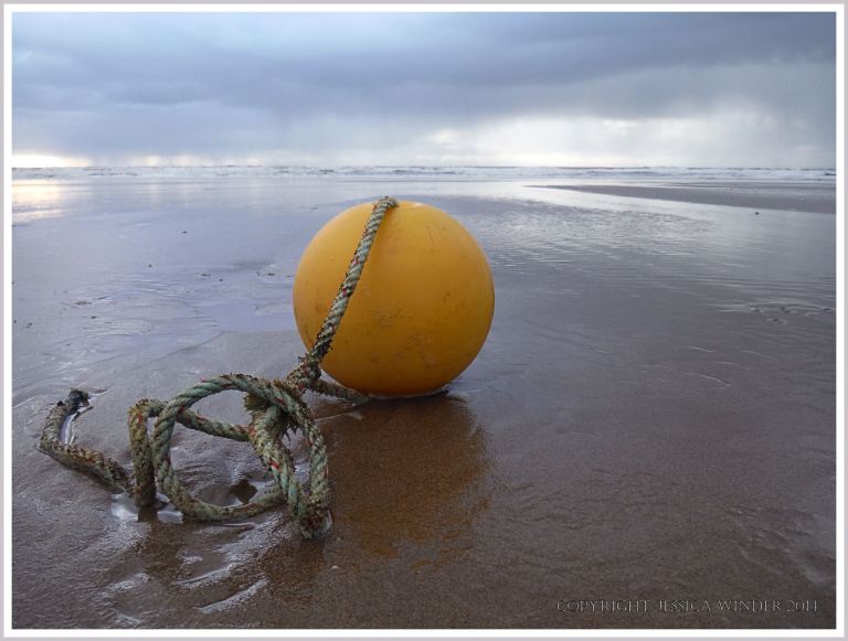 Yellow fishing float with rope washed up on sandy beach