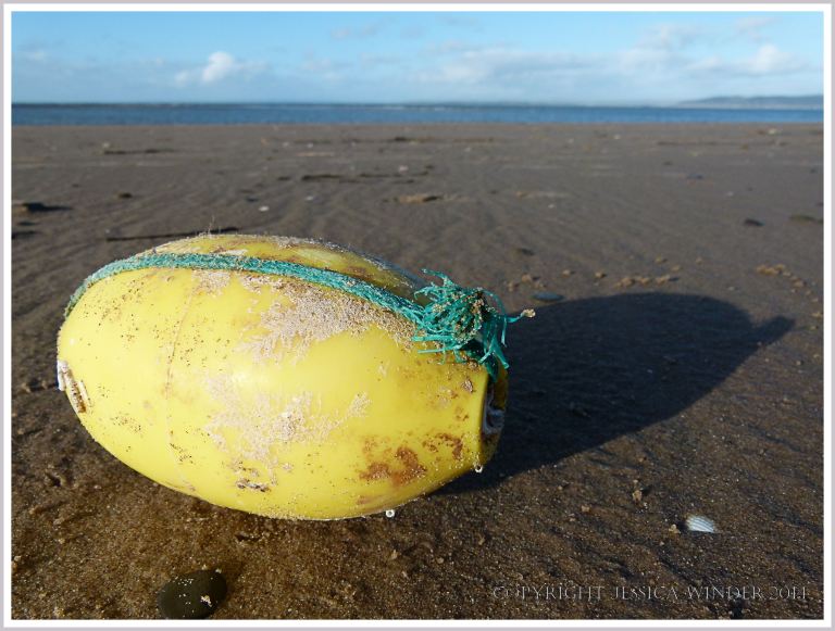 Ovoid yellow plastic fishing float with green rope on sand