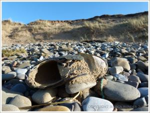 Old shoe full of sand washed up on beach stones