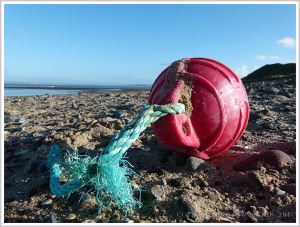 Red plastic fishing float with green rope washed ashore at Whiteford Sands
