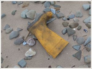 Yellow wellington boot washed up on sand and pebbles