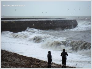People looking at storm waves near the Cobb wall at Lyme Regis in Dorset