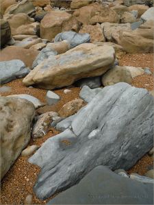 Boulders on the seashore with orange gravel
