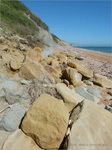 Sedimentary rock beach boulders at the base of clay cliffs.