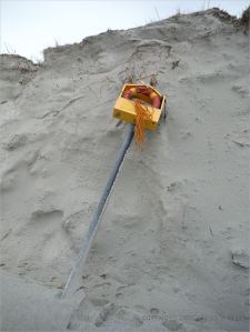 Fallen life belt in container on post on eroded beach sand dune