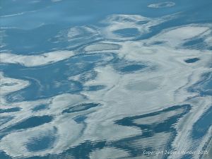 Seafoam, water texture and cloud reflection pattern in the bow wave of a ferry crossing the still waters of the Northumberland Strait in Canada