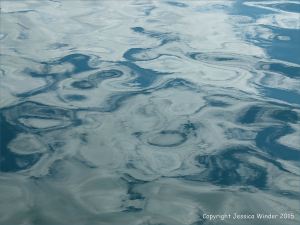 Seafoam, water texture and cloud reflection pattern in the bow wave of a ferry crossing the still waters of the Northumberland Strait in Canada