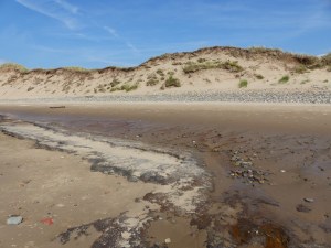 Red liquid draining from the beach at Whiteford Sands