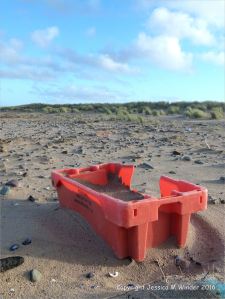 Red plastic flotsam fishing crate washed ashore