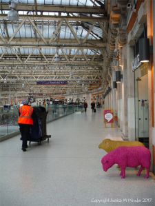Two colourful sheep looking lost at a train station