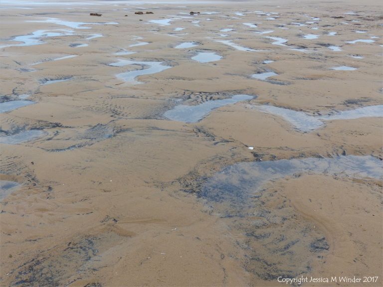 Water-filled sandy hollows on Rhossili beach, Gower