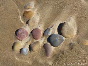 A natural arrangement of coloured pebbles in damp but drying sand