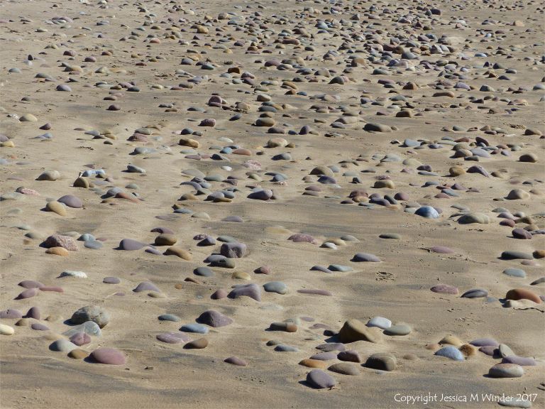 Coloured beach stones in damp sand between high and low tide levels