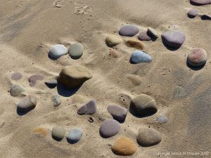 Coloured beach stones in damp sand between high and low tide levels