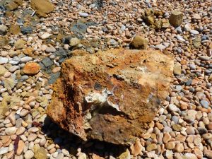 A rusty rock with crystals lying on a pebble beach