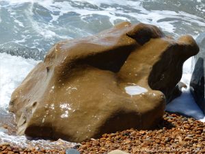 Strange shaped boulder splashed by waves on the pebble beach at Seatown in Dorset
