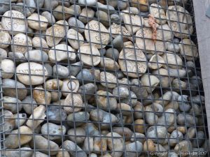 Natural pebbles and decorative hand-made ceramic pebbles in wire cages called gabions