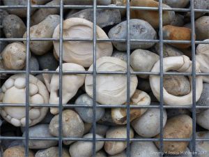 Natural pebbles and decorative hand-made ceramic pebbles in wire cages called gabions