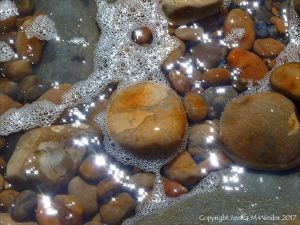 Colourful wet pebbles in the breaking waves at the waters' edge on the beach