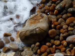 Colourful wet pebbles in the breaking waves at the waters' edge on the beach