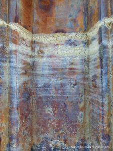 Pattern of dried sea foam tide lines on a rusty iron pier