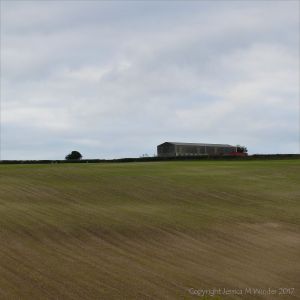 A barn on the crest of a hill under an overcast sky with newly sown field below