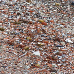 Detail of the composition of an urban shore along a tidal river where water-worn historical building and domestic debris is mixed with natural flints and stones.