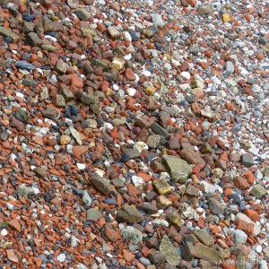 Detail of the composition of an urban shore along a tidal river where water-worn historical building and domestic debris is mixed with natural flints and stones.
