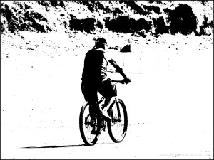Black and white image of a man cycling across a beach
