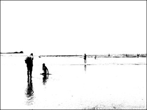 Black and white image of people on the water's edge at the beach