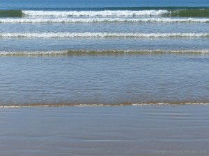 Rhossili Beach on a summer day showing waves lapping onto the shore