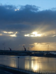Early light breaking through winter clouds over docks with cranes