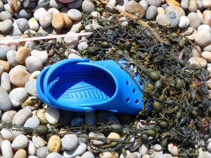Blue Croc shoe and seaweed washed up on a pebble beach