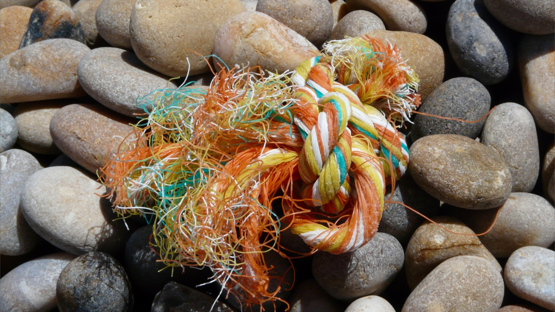 Orange multicolour knotted rope washed up on a pebble beach