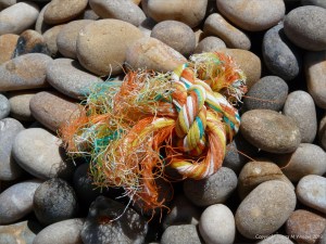 Orange multicolour knotted rope washed up on a pebble beach