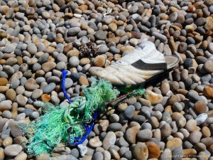 White trainer shoe and green rope washed up on a pebble beach