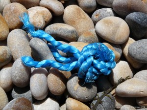 Piece of blue knotted rope washed up on a pebble beach