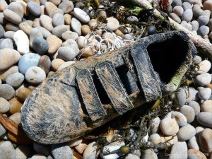 Black shoe with hydroid encrustation washed up on a pebble beach