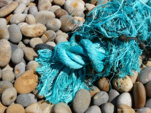 Piece of green knotted rope washed up on a pebble beach