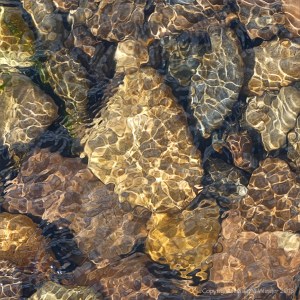 Natural patterns of reflected light on water flowing over pebbles