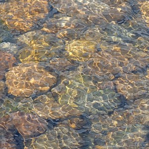 Natural patterns of reflected light on water flowing over pebbles
