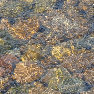 Natural patterns of reflected light on water flowing over pebbles